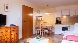 Un espacio habitable compacto con kitchenette, zona de comedor y área de estar con televisión y muebles de madera.