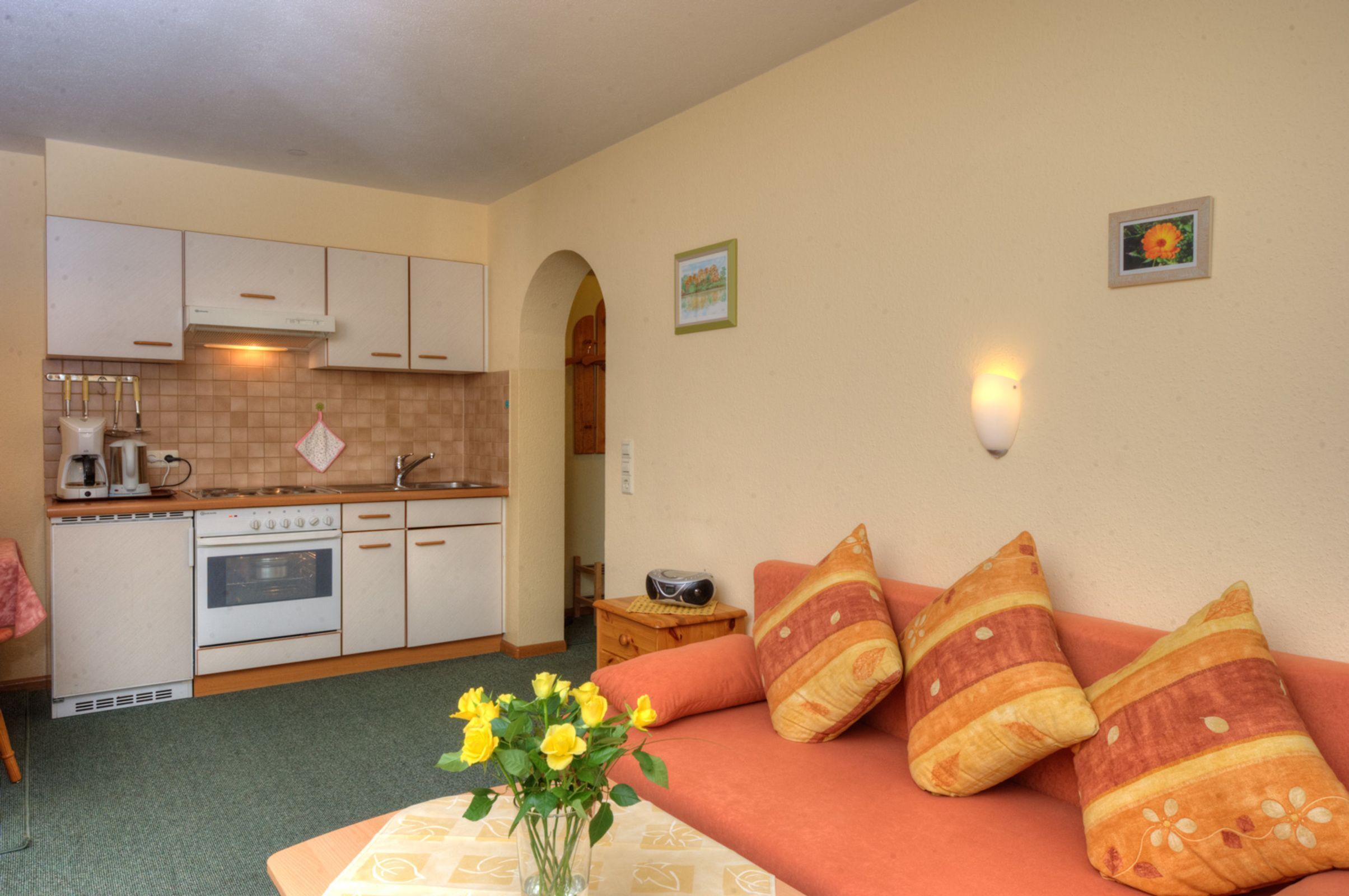A compact kitchen with white appliances, a dining area with a table and chairs, and a sofa with patterned cushions.