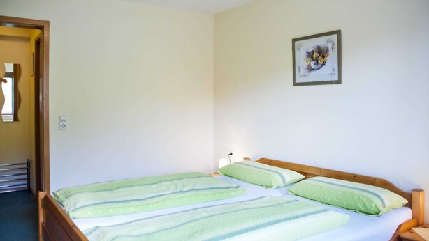 Habitación individual con una cama de madera, una mesita de noche y una lámpara de pared.