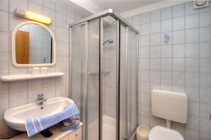A bathroom with a glass-enclosed shower, a sink with a towel, and a toilet.