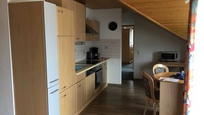 A compact kitchen with wooden cabinets, a microwave, and a dining area with a chair and table.