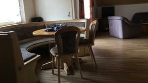 A cozy room with a wooden ceiling, a round table with chairs, a sofa, and a television.
