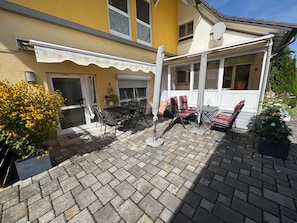 A patio with outdoor furniture, a covered seating area, and a yellow building with a satellite dish.