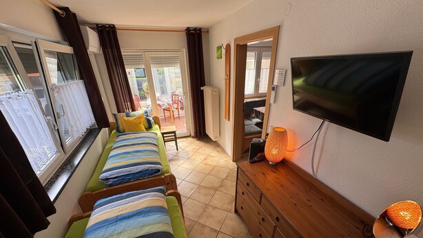 Habitación con dos camas individuales, televisión, cómoda de madera y puerta corrediza de vidrio que da a un espacio exterior.
