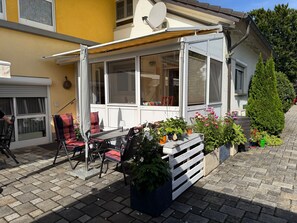 A covered patio with outdoor furniture, a table, and potted plants.