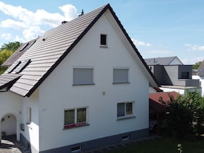 A white two-story house with a sloped roof, a small window, and a garage door.