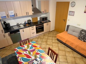 A compact kitchen with a microwave, stove, and sink. There's a dining table with chairs and a bed with an orange bedspread. - Non-smoking vacation apartment Martha-Stephanie, 2 bedrooms, 4 persons - (Rust)