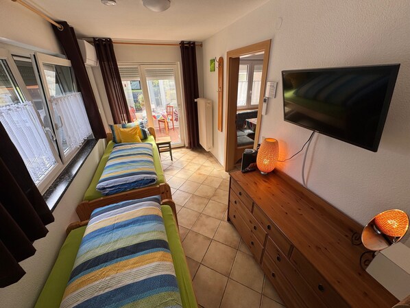 Habitación con dos camas individuales, televisión, cómoda de madera y puerta corrediza de vidrio que da a un espacio exterior.