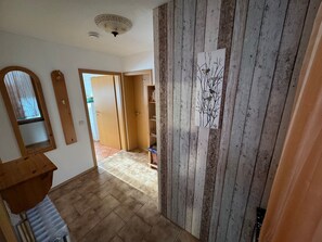 A hallway with wooden paneling, a wooden door, a mirror, and a shelf with books.