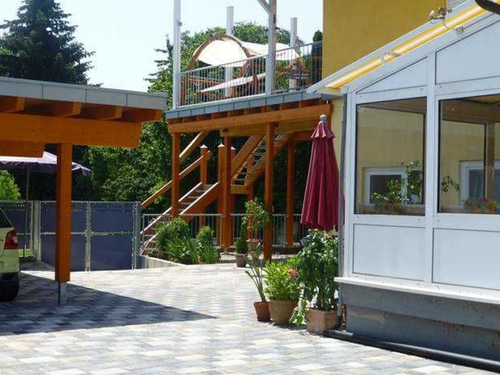 A covered outdoor area with a wooden deck, potted plants, and a building with large windows.