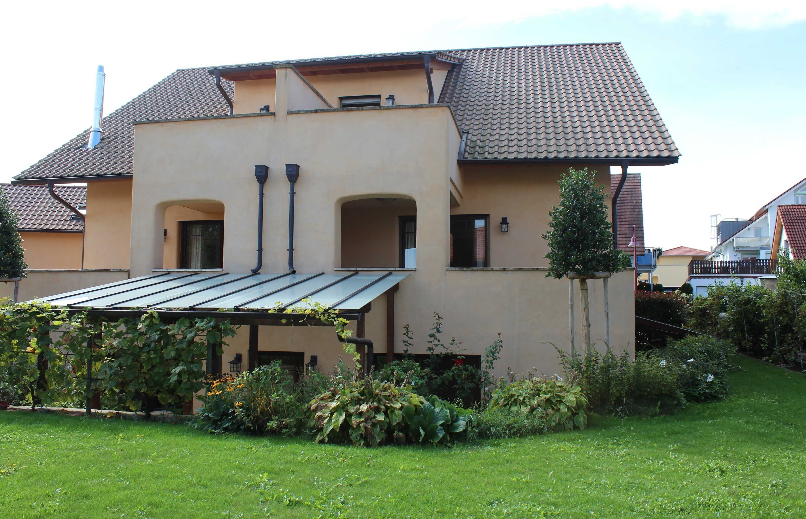 A two-story house with a tiled roof, a covered patio, and a garden.