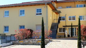 A yellow building with multiple windows, a staircase, and a paved entrance area with potted plants.