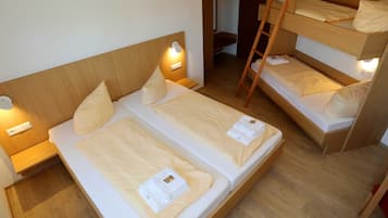 A room with two single beds and a bunk bed, wooden headboards, bedside lamps, and a wooden ladder.