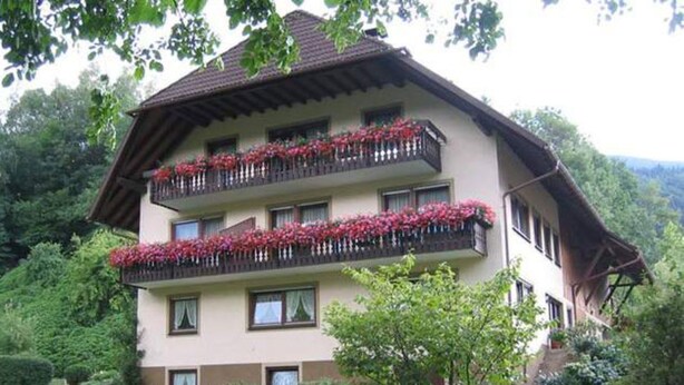 A multi-story building with balconies adorned with red flowers, surrounded by lush greenery and a well-maintained garden. - Vacation apartment Kapellenblick, 45sqm, 1 bedroom, max. 3 persons, 1 - 3 (Simonswald)