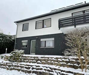 Une maison à deux étages avec un escalier en pierre menant à l’entrée, le tout entouré de neige.