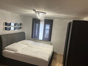 Une chambre à coucher comprenant un lit, un radiateur, une fenêtre avec des rideaux, un ventilateur de plafond et un luminaire fixé au mur.