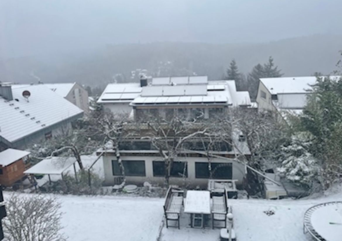 A residential area with multiple buildings, some with solar panels, and a snow-covered landscape.