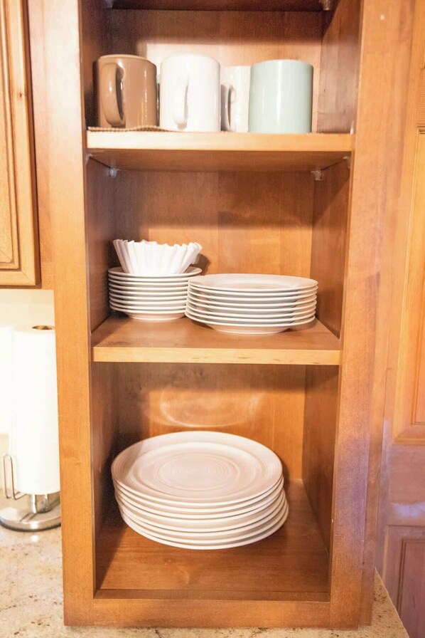 Un mueble de madera con tres estantes, cada uno con pilas de platos blancos y algunos vasos blancos.