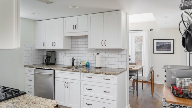Una cocina moderna con armarios blancos, encimeras de granito y una cafetera.