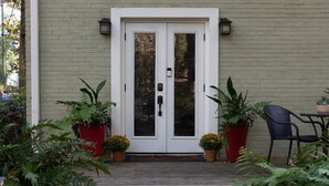 Puerta principal con un panel de vidrio, dos macetas, una silla negra y una mesa.