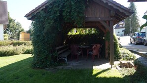 Une pergola en bois, avec une table et des chaises en dessous, entourée de verdure.