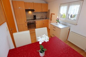 A compact kitchen with wooden cabinets, a dining table with a red tablecloth, and a window with curtains.