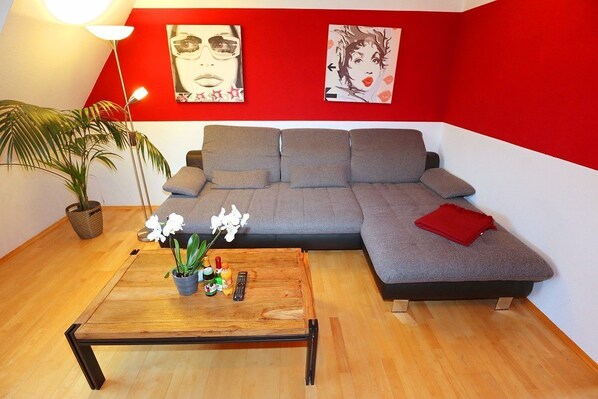 A modern living room with a grey sectional sofa, a wooden coffee table with a potted plant, and a red throw on the sofa.