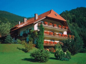 A two-story chalet with balconies, surrounded by greenery and a mountainous backdrop. - Apartment Talblick - Mosertonihof (Elzach)