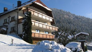 A multi-story building with balconies, a sign indicating 'Pension,' and snow-covered surroundings.