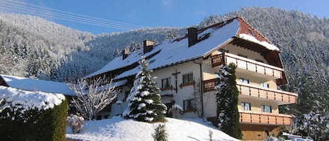 Ein mehrstöckiges Gebäude mit Balkonen, umgeben von schneebedeckten Bäumen und einem Berg im Hintergrund.