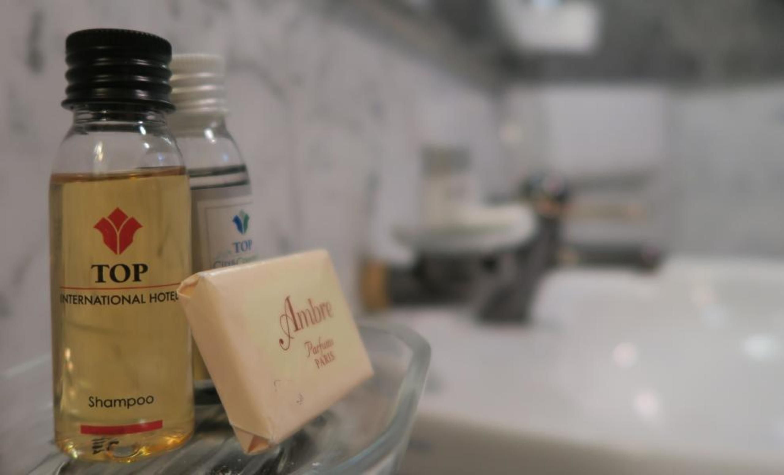 A bathroom with a glass shelf holding a shampoo bottle, a bar of soap, and a bottle of lotion.