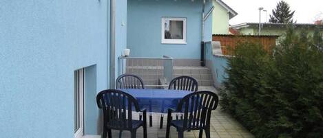 A blue exterior wall, a tiled patio, a table with four chairs, and a small window.