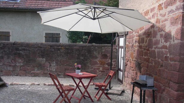 Une terrasse avec une table et des chaises, un parasol et une petite table avec un coffre.