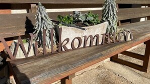 A wooden bench with a metal sign that reads "Willkommen" and two small trees. - Mockhof - Bachhüsliblick (Waldkirch)