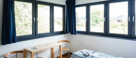 A small, bright room with a bed, a desk, and two chairs.