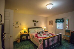 A bedroom with a bed, bedside tables, a chair, a window with curtains, and a door.