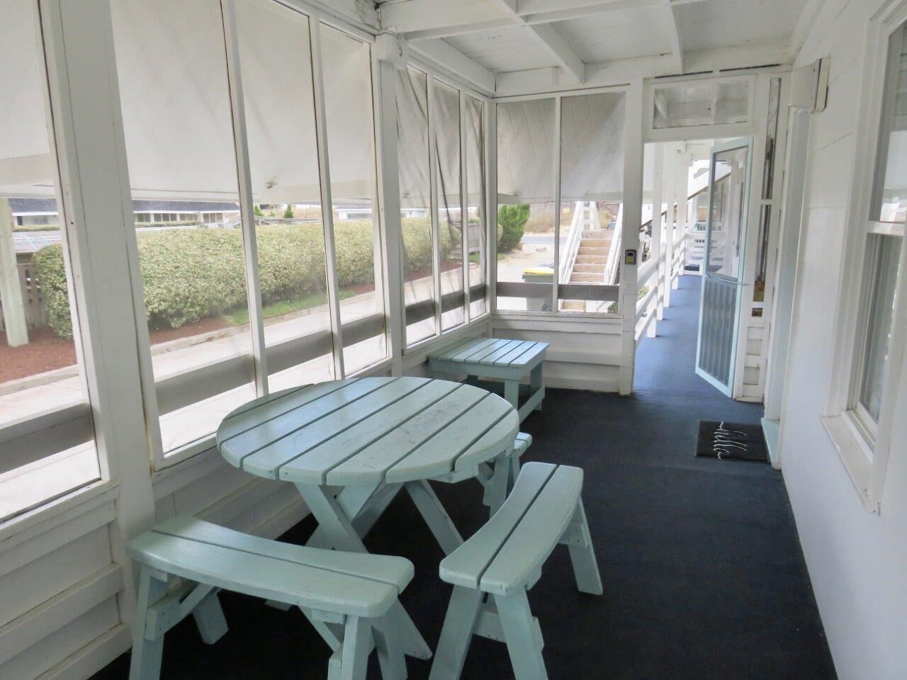 A covered outdoor area with picnic tables and benches, large windows, and a view of a building and greenery outside.