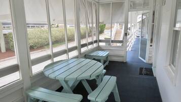 A covered outdoor area with picnic tables and benches, large windows, and a view of a building and greenery outside.