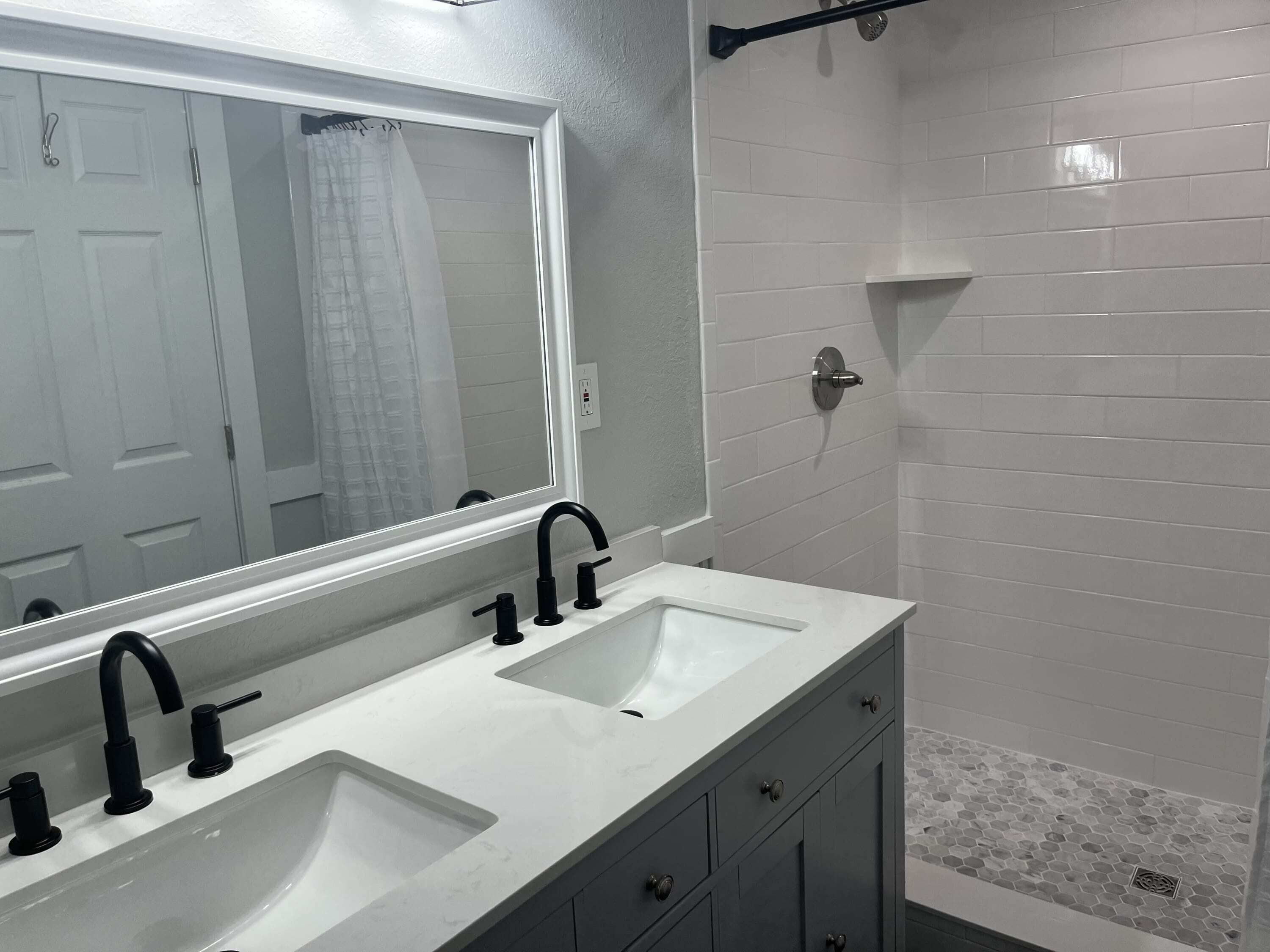 A bathroom with two sinks, a large mirror, and a shower area.