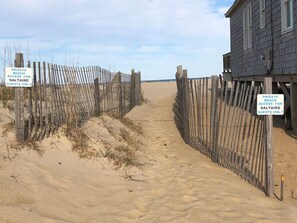 Un sentier de sable qui longe la plage et mène à une structure en bois, sur laquelle est apposée une pancarte indiquant que l’accès à la plage est réservé aux clients de l’établissement.