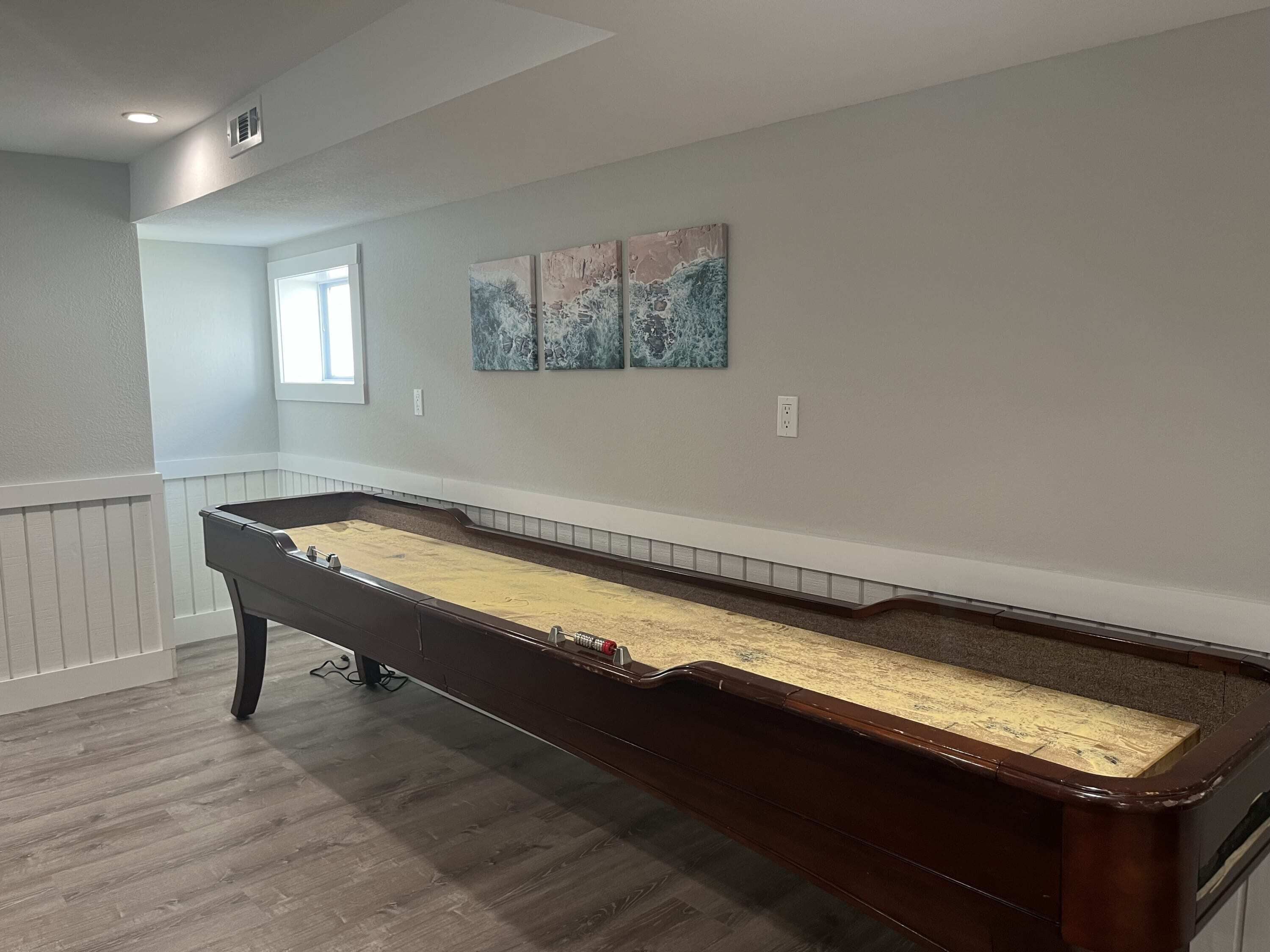 A pool table in a room with white walls, a window, and three abstract paintings.