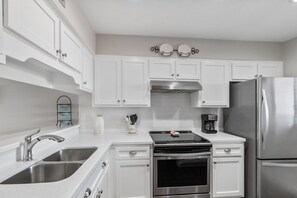 A modern kitchen with white cabinets, stainless steel appliances, a double sink, and a coffee maker.