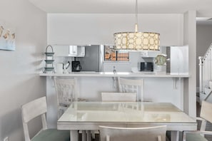 Une cuisine moderne avec des meubles blancs, une table à manger en verre et un luminaire suspendu.