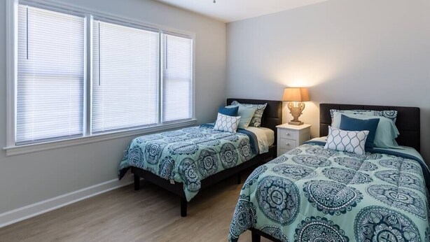 A bedroom with two beds, a ceiling fan, and a window with blinds. - Cozy Coastal Blue Crab Bungalow- Outdoor Shower- Fully Fenced Yard Isle of Palms (Isle of Palms)