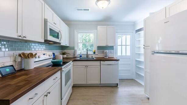 Una cocina moderna con armarios blancos, encimera de madera, microondas, estufa y refrigerador.
