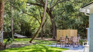 Un patio trasero con una terraza de madera, mobiliario exterior y una hamaca.