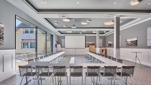 Un salón de conferencias con una larga mesa, sillas, una pantalla de proyector y un amplio ventanal.