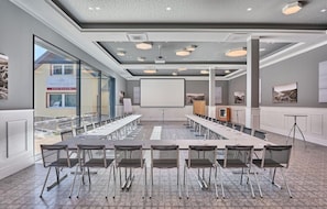 Ett konferensrum med ett långt bord, stolar, en projektorduk och ett stort fönster.