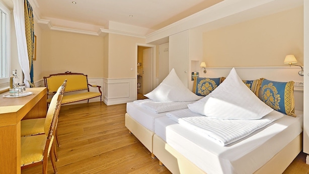 Una habitación de hotel con una cama, un escritorio con una silla y un baño visible a través de una puerta abierta.