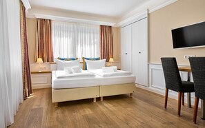 Ein Hotelzimmer mit Bett, Nachttischen, Fernseher und Schreibtisch mit Stühlen.